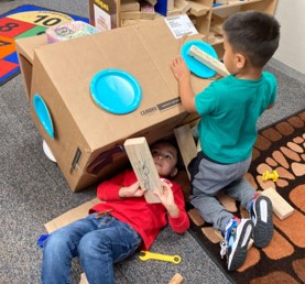 Young children at Eagleton Elementary School work together to build a structure out of cardboard boxes, wooden planks, and paper plates.